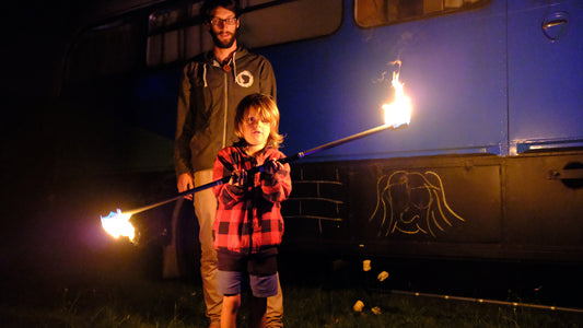 A young child spins a fire spin staff with an adult standing watch behind him