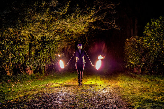 A person spins fire poi on a dark, rainy night with trees in the background