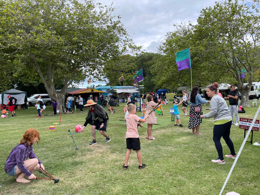 A group of people play with devil sticks, juggling sticks at a park on a sunny day