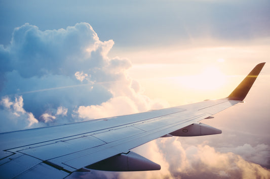 A plane wing in the clouds with the sun peeking through