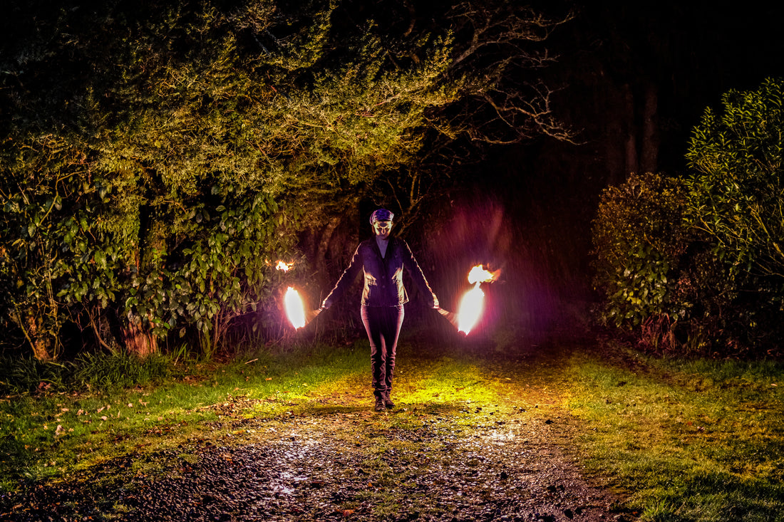 A person spins fire poi on a dark, rainy night with trees in the background