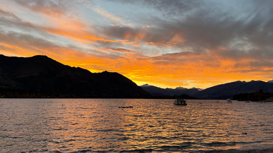 An orange sunset sky above darkly silhouetted mountains with a glistening body of water