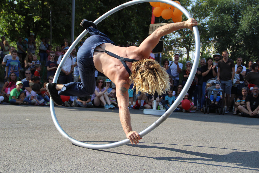 A person spins upside down on a large cyr wheel with a captivated audience in the background