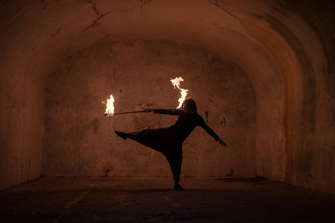 A person stands with one leg held out to the side, holding a lit fire staff in one of their hands