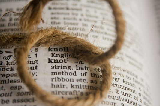A knotted brown string sits on a dictionary close up of the word knot